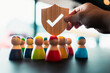 © sommart - Hand holding wooden shield with check mark protecting diverse wooden people figures, symbolizing group protection, insurance, teamwork safety, and community care.