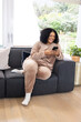© Wavebreak Media - African American mid adult woman sitting on dark gray sofa in living room using smartphone
