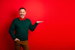 © deagreez - Playful mature man in green sweater presents against red backdrop smiling and posing for festive christmas themed stock photo