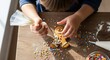 © Таня Андреева - A close-up, overhead shot of a child's hands using a piping bag to decorate a gingerbread man cookie with white icing and colorful sprinkles on a wooden table.