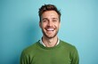 © Vadym - Smiling man poses in studio shot. Brunet guy wears green jumper. Handsome model laughs with toothy smile, expressing joy. Positive man in casual wear. Isolated studio portrait on cyan background.