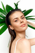 © VICHIZH - Young woman with clear skin posing gracefully against green foliage, showcasing natural beauty and serenity, perfect for wellness themes.