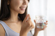 © hidez - Close-up of a Woman Holding a Supplement Pill and a Glass of Water