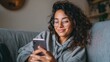 © Johannes - happy 20s young woman watching social media videos looking at smartphone relaxing on couch smiling hispanic girl enjoying using online mobile apps doing online shopping on cell phone at home no logos