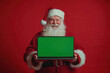 © vasyl pshyk - Santa Claus multitasking with a laptop against a festive red backdrop for holiday marketing creativity