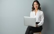 © ling - Young business woman posing isolated over grey wall background sitting on stool using laptop computer. High quality