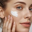 © JS - 젊은 여성이 깨끗한 피부에 흰색 보습 크림을 바르며 정면을 응시하는 클로즈업 뷰티 샷