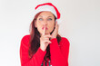 © tetxu - A woman wearing a festive red sweater and a Santa hat, holding a finger to her lips