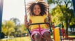 © Vasiliy - Happy young African American girl with curly hair on a swing at the playground. Cheerful child playing outside on a sunny summer day. Childhood joy and recreation concept
