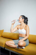© Westend61 - Woman sitting on sofa drinking water after home workout