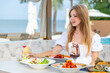© TravelMedia - Young woman in beachside restaurant enjoying summer meal with drinks, surrounded by tropical scenery. Leisure, vacation, food, and drink concept.