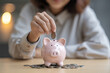 © Alena - Beautiful Asian businesswoman insert coins in a pin piggy bank on the table. saving money, investment, currency concept