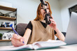 © True Pixel Art - A young woman speaks into a condenser microphone on a boom arm while writing in a notebook beside a laptop in a modern studio, warm light, shallow depth of field