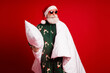 © deagreez - Santa in cozy pajama cape holds pillow smiles under red background for Christmas fun and festive season shopping dream