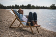 © Westend61 - Senior man with coffee cup relaxing on deck chair by sea