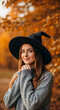 © NeuroCake - A young woman in a witch hat and cozy sweater. Halloween costume portrait in an autumn park. Celebrating the fall holiday season