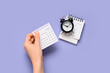 © Pixel-Shot - Female hand with calendar and alarm clock on purple background