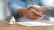 © olga_demina - Real estate agent and client shaking hands after signing a contract for the purchase of a new house, miniature house model and contract on the table