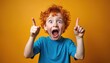 © Pete - Excited redhead boy shouts pointing fingers up with joy and amazement. Surprised ginger kid with open mouth has a great idea. Happy emotional child shows a eureka moment on orange background.