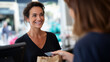 © Sergio IQstock - Happy female customer paying with bank card at checkout counter, receiving paper bag from shop assistant, friendly service, modern retail atmosphere, bright daylight, consumer life