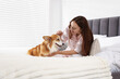 © New Africa - Pet friendly hotel. Smiling woman with her cute Welsh Corgi dog on bed indoors