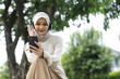 © eakgrungenerd - Muslim women in hijab wearing headphones, enjoying music or podcast on smartphone outdoors. Relaxing digital lifestyle, modern technology and leisure concept in natural park.