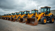 © Pete - Row of yellow heavy equipment front loaders parked outdoors. Industrial vehicles ready for work. Construction machines on the lot ready for rent or sale.