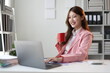 © Wasan - Smiling businesswoman drinking coffee at office desk.