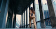 © serg - Rear view of confident businesswoman with long flowing hair, wearing tailored formal suit, walking up outdoor stairs while holding laptop in one hand, approaching modern office building