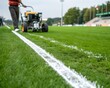 © towsif - Person using a line marking machine to paint white lines on a green grass sports field outdoors