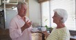 © vectorfusionart - Holding cups, senior couple in pink shirt and striped top talking in home kitchen, potted plants