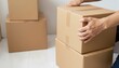 © Elenba - Cardboard boxes, showing moving boxes in stack against neutral wall. Moving boxes symbolize relocation with stacks of sealed packages and human hands carefully stacking. For a moving boxes concept,