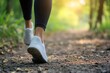 © Татьяна Евдокимова - Person's legs and white sneakers taking a step on a sunlit walking trail, symbolizing health, fitness, and outdoor activity