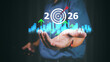 © PRIM - Businessman holding virtual 2026 with rising arrows and target icon, symbolizing new year business goals, strategic vision, future growth, success planning and performance improvement.