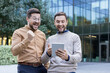 © Liubomir - Two excited business colleagues celebrating triumph, looking at a digital tablet outdoors, standing in front of a modern glass building, expressing success and joy