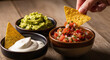 © Soft Studio - Hand dipping nacho chip into salsa with guacamole and sour cream bowls