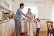 © Stockphotodirectors - A happy family shares a joyful moment as they dance together in their bright kitchen. The parents hold hands with their excited child, creating a lively atmosphere.