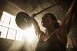 © EricMiguel - Determined female athlete performing overhead barbell weightlifting in a sunlit industrial gym - intense workout, sweat, strength and focus