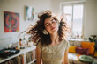 © EricMiguel - Young woman with headphones enjoying music at home — curly hair flowing in sunlight, dancing carefree in a cozy living room with vinyl turntable