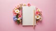 © Jotch - Soft pastel pink notebook with a small white pencil and colorful flowers arranged around it