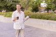 © Tj - Senior professional man walking outdoors with a hot coffee cup and modern laptop, contemplating or thinking about business while enjoying a moment of remote work or a break in the park