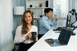 © InfiniteFlow - Profile smiling beautiful Asian businesswoman looking camera while holding cup to pose at modern office on working desk. Blurry background man colleague analyzing data market report on pc. Infobahn.