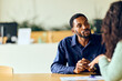 © bnenin - African-American Man In Navy Shirt Talks With Colleague At Office Desk