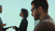 © Videophilia - Focused man wearing glasses and a beard, looking down and concentrating during a blurred business meeting with colleagues in the background, showing professionalism and dedication