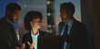 © Videophilia - Diverse business colleagues working together, discussing a project on a laptop in a modern office at night, demonstrating teamwork and professional collaboration