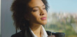 © Videophilia - Young african american businesswoman drinking coffee, relaxing herself during a break, looking outside a window with an urban background, thinking about work and having ideas