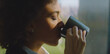 © Videophilia - Woman with eyes closed slowly sipping from a dark coffee mug, finding peace and relaxation while standing by a window, bathed in warm morning sunlight