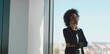 © Videophilia - Afro businesswoman making a phone call, standing by large window, having remote business conversation with client while overlooking city view from corporate office