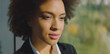 © Videophilia - African american businesswoman with curly hair looking thoughtful and focused, standing in a professional setting with natural sunlight highlighting her face, representing success and determination