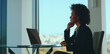 © Videophilia - Professional businesswoman sitting at office desk, resting chin on hand and thoughtfully looking out a large window at the city skyline, demonstrating contemplation and future planning